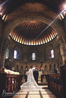 bride and groom Kneeling in church bathed in sunlight 